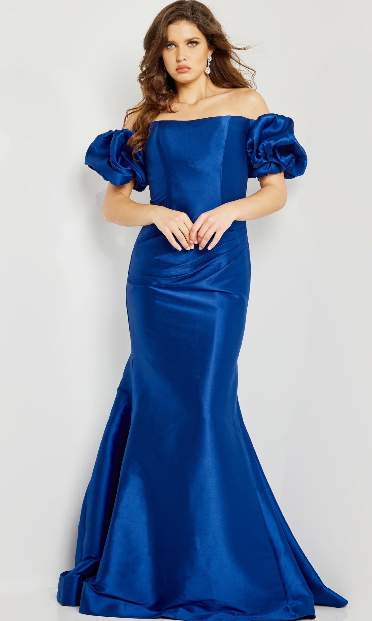 A woman wears the Jovani 08361 Puff-Sleeve Mikado Evening Dress in royal blue, featuring off-the-shoulder puffed short sleeves and a fitted, floor-length skirt.
